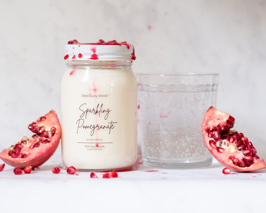 Jar of 'Sparkling Pomegranate' candle with pomegranate pieces and sparkling water on a white background