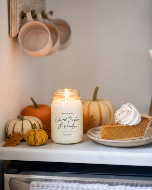 Deliciously Wickt Whipped Pumpkin Marshmallow 16 oz mason jar soy candle lit beside pumpkins and a slice of pumpkin pie topped with whipped cream.
