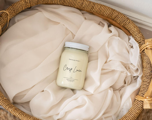 Candle Jar labeled 'Crisp Linen' on a white fabric background inside a woven basket