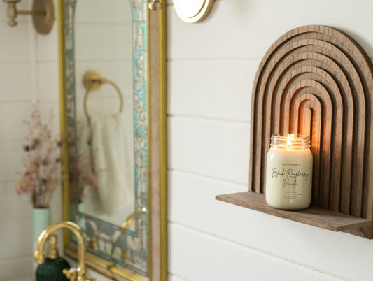 Mason jar candle scented black raspberry vanilla on a wooden shelf next to a mirror in a bathroom setting