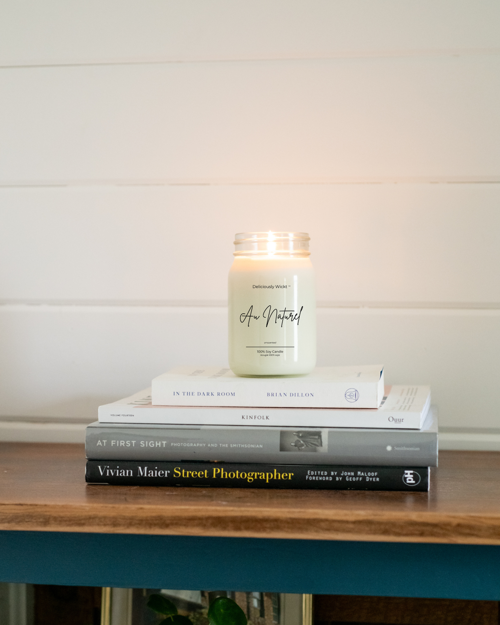 Candle labeled 'Au Naturel' on a stack of books with a white wall background