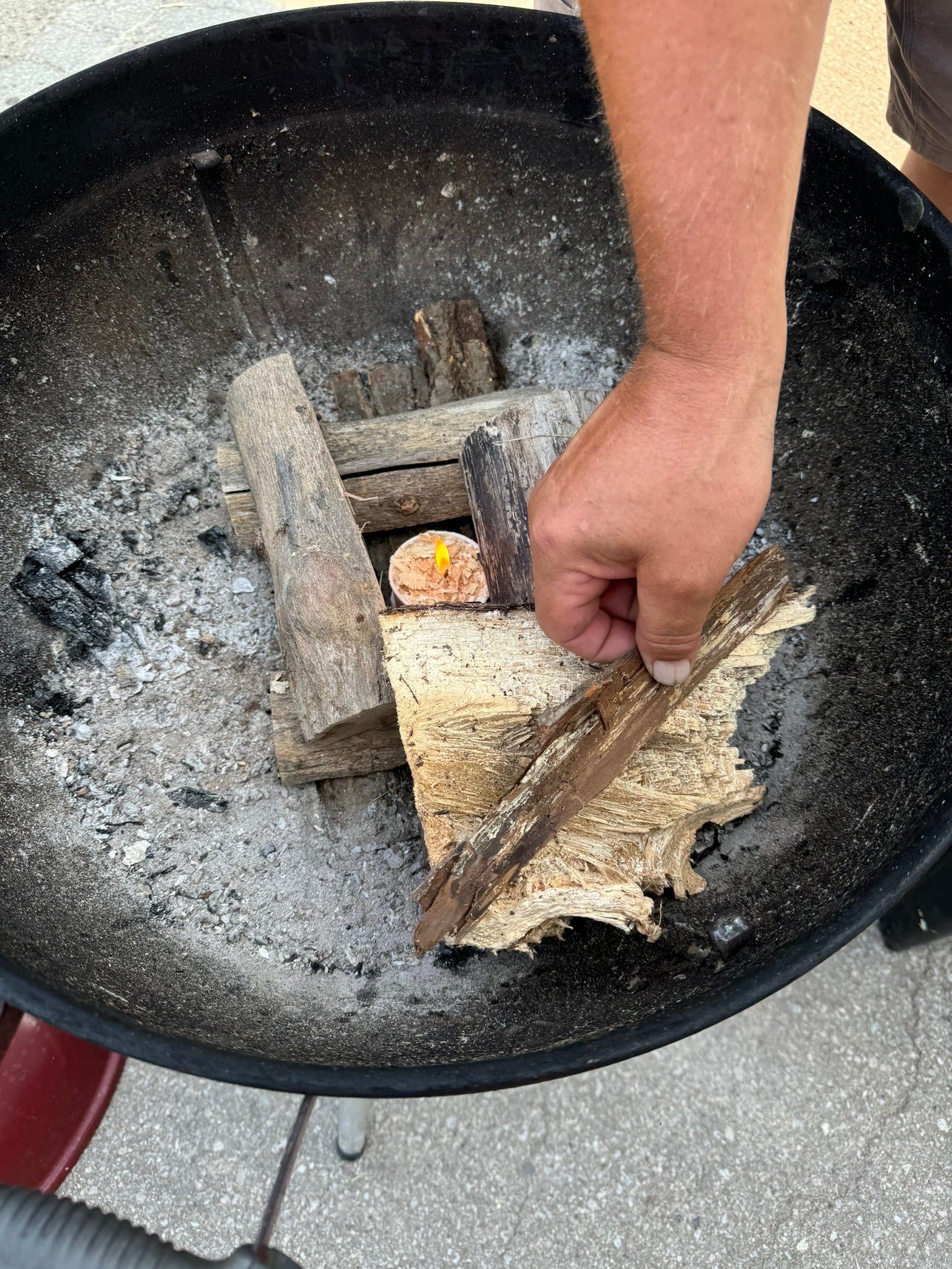 Person holding wood over a fire pit with burning logs inside, using firestarter pods