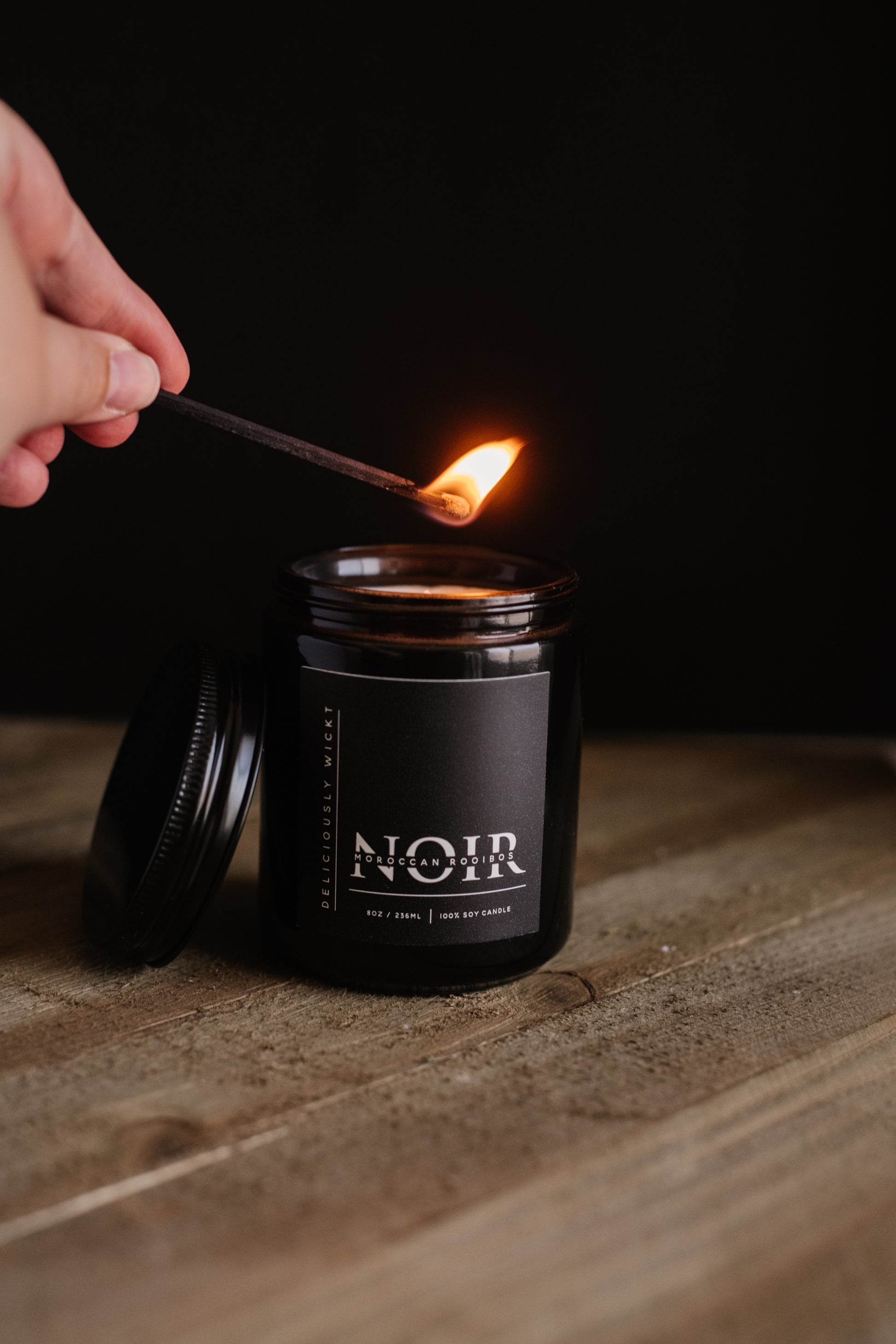 Deliciously Wickt all black long stick safety match being used to light a black NOIR soy candle.