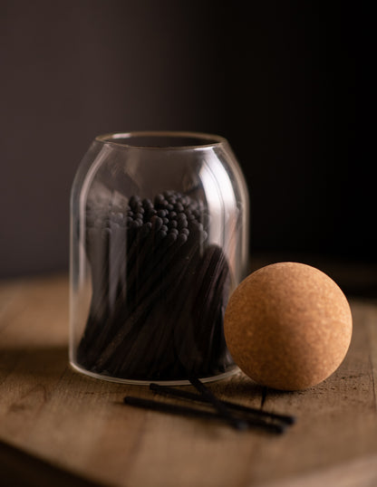 Deliciously Wickt all black long stick safety matches in a clear glass jar with round cork stopper.