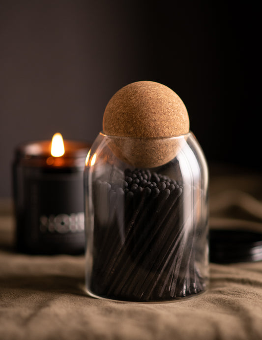 Deliciously Wickt all black long stick safety matches in a glass jar displayed beside a lit NOIR soy candle.
