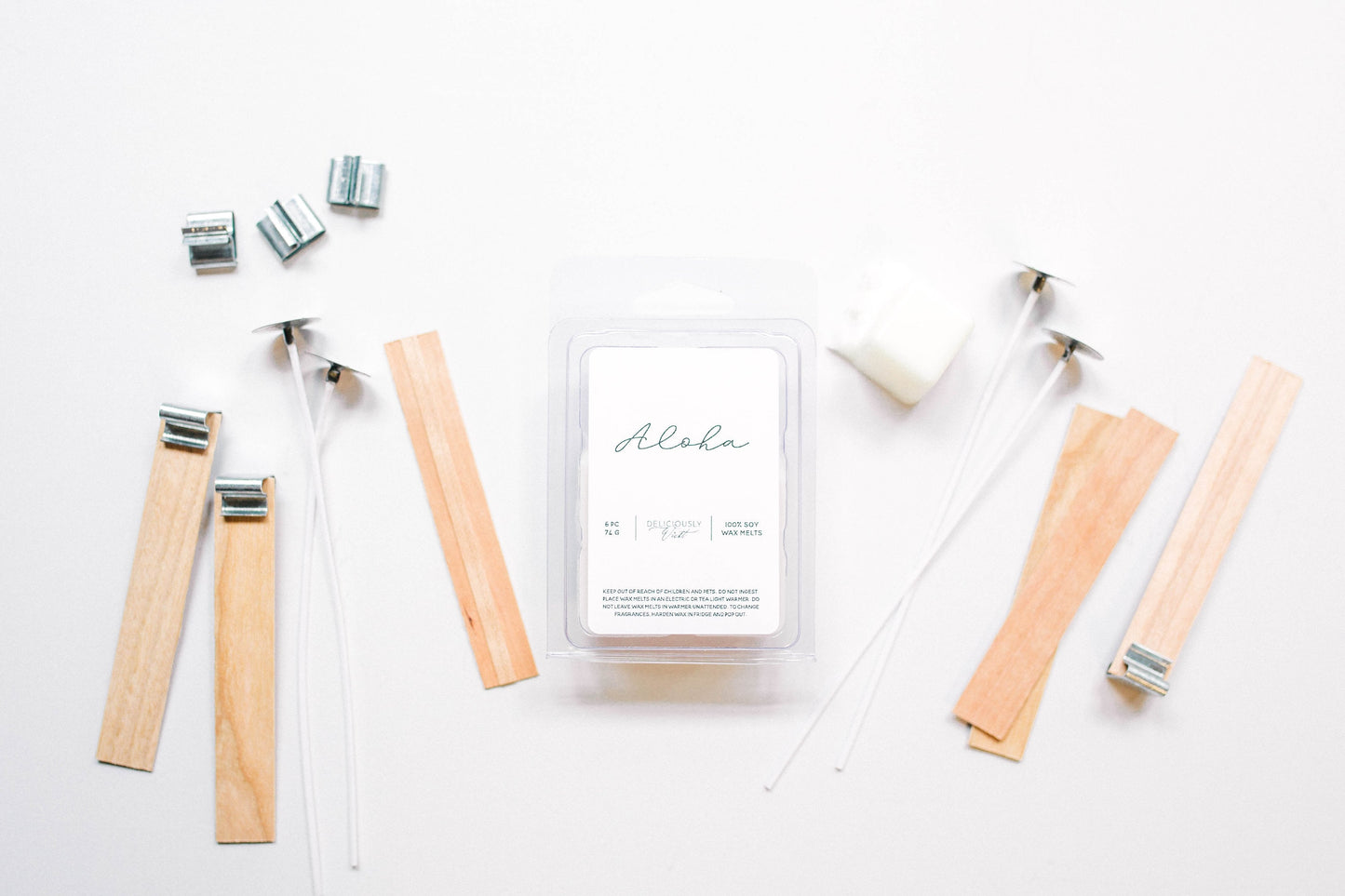 Deliciously Wickt Aloha soy wax melts surrounded by wooden sticks and candle-making accessories on a white background.