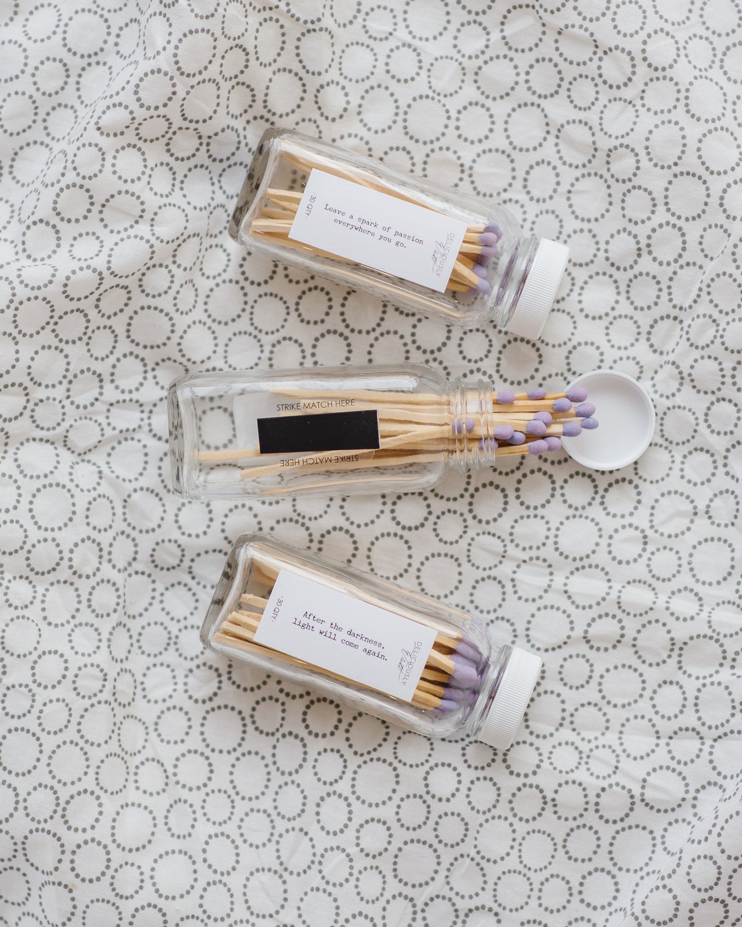 Three Deliciously Wickt glass bottles of long stick safety matches with assorted match-tip colours on patterned fabric.
