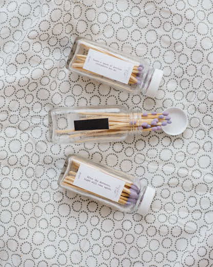 Three Deliciously Wickt glass bottles of long stick safety matches with assorted match-tip colours on patterned fabric.