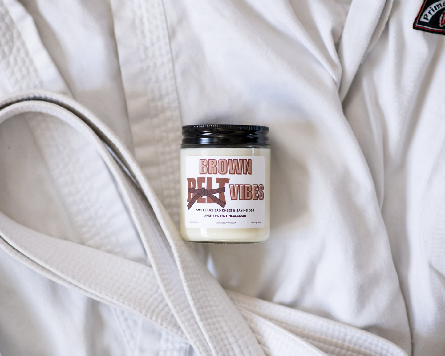 Brown Belt Vibes Jiu-Jitsu soy candle displayed on a white gi