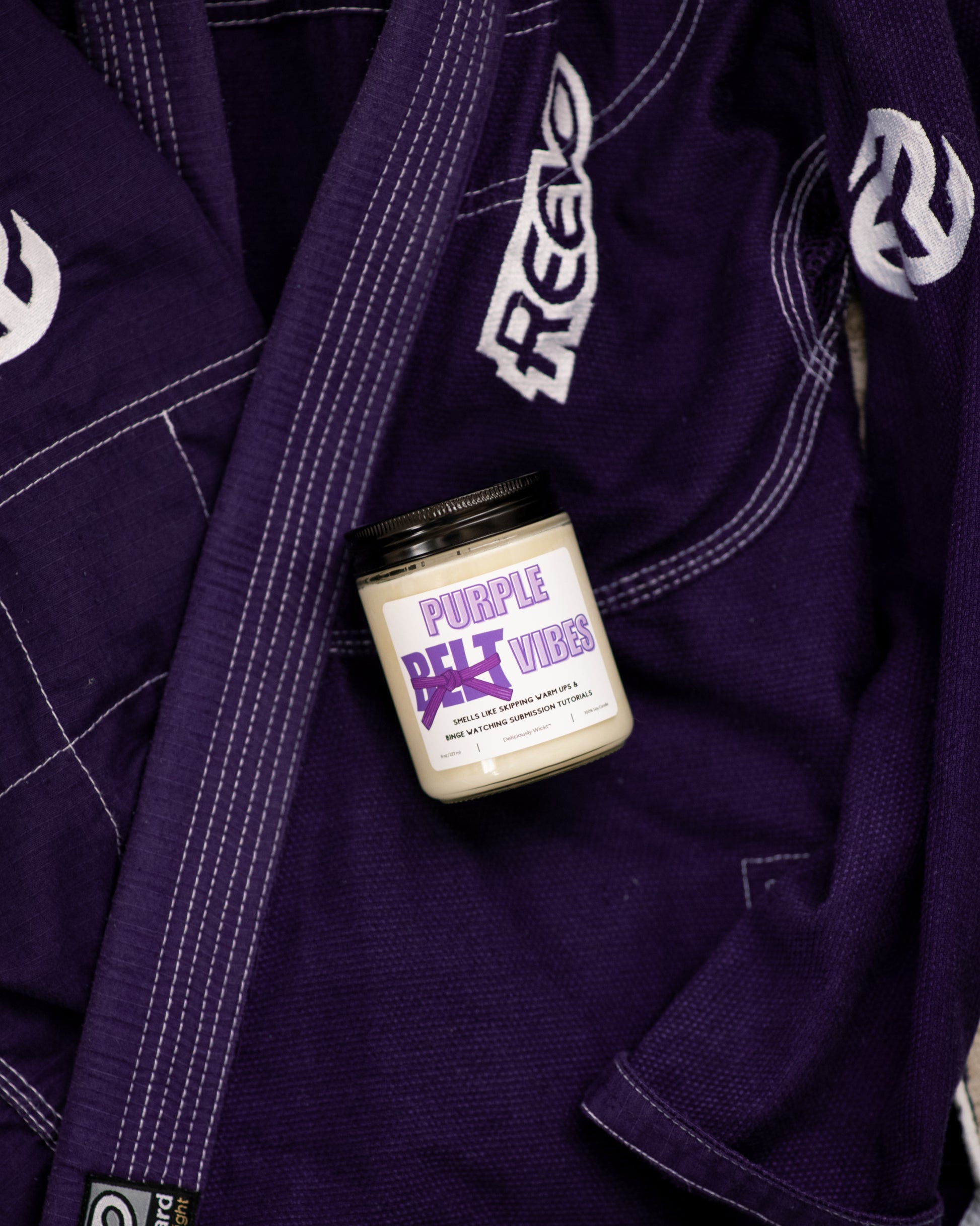 Belt Color Vibes Jiu-Jitsu soy candle with purple belt label displayed on a purple gi