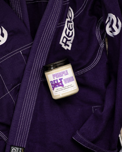 Belt Color Vibes Jiu-Jitsu soy candle with purple belt label displayed on a purple gi