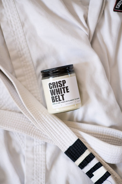 Crisp White Belt Jiu-Jitsu soy candle with “Smells like your life is about to change” label on a white gi
