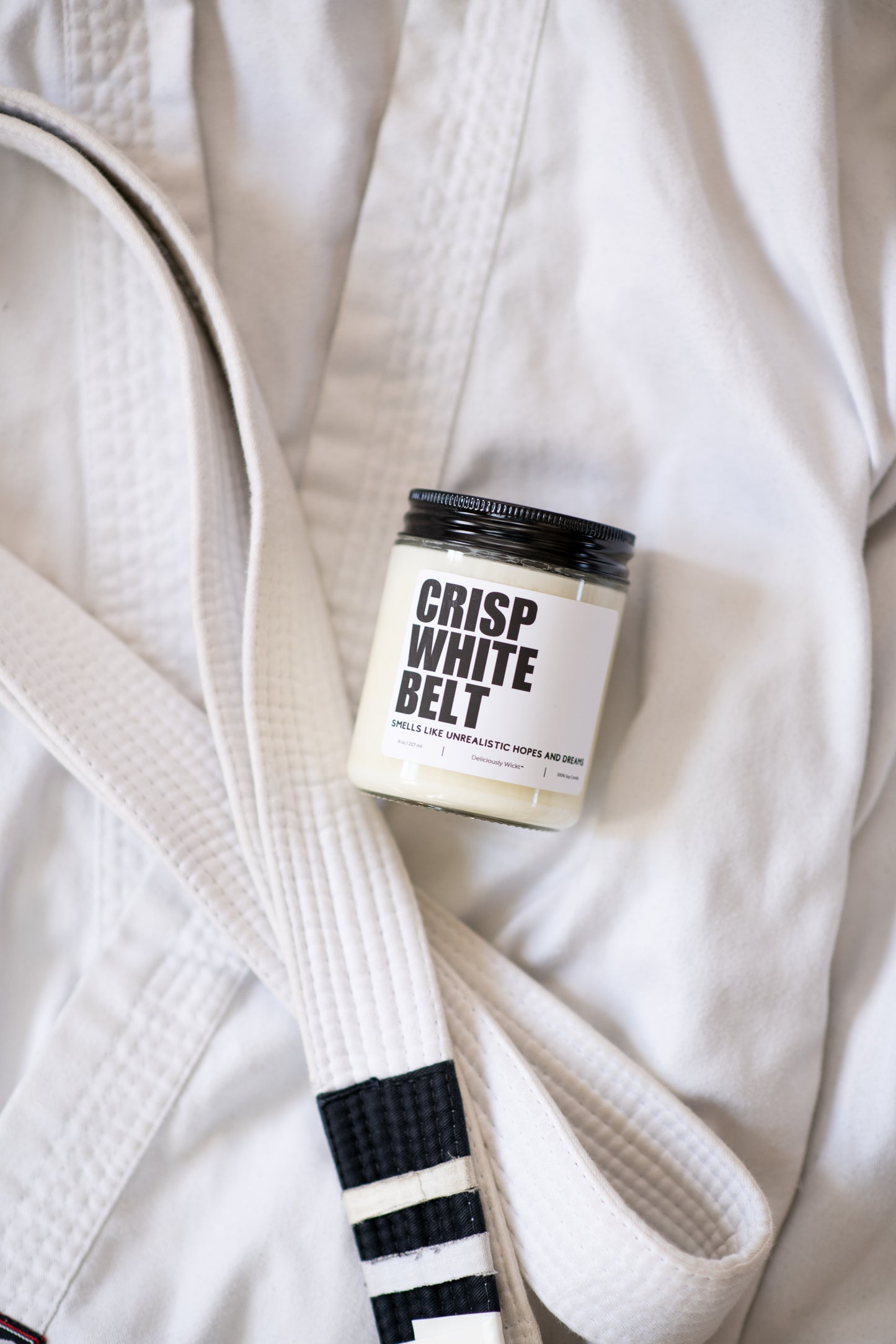 Crisp White Belt Jiu-Jitsu soy candle with “Smells like unrealistic hopes and dreams” label on a white gi