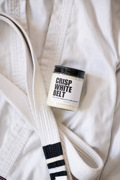 Crisp White Belt Jiu-Jitsu soy candle with “Smells like unrealistic hopes and dreams” label on a white gi