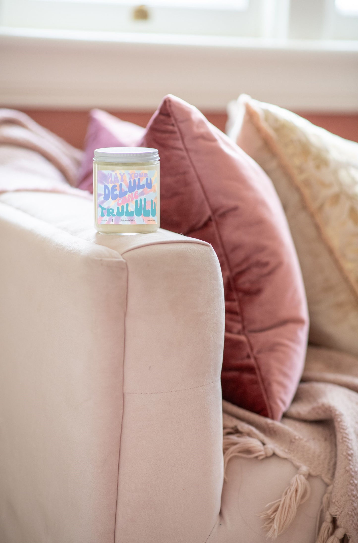 Deliciously Wickt Delulu Come Trululu 8 oz soy candle displayed beside a pink upholstered chair.