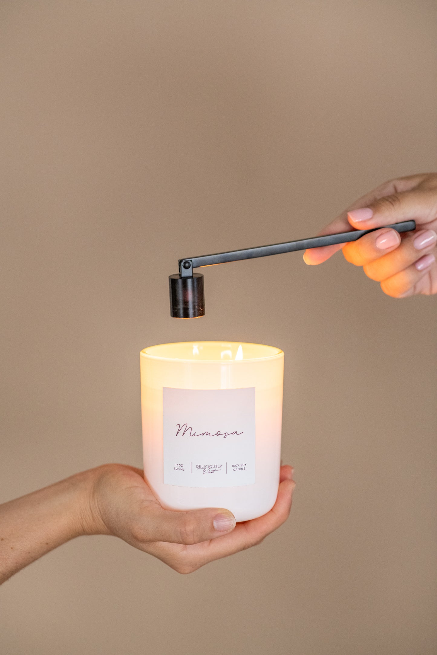 Deliciously Wickt glossy white 17 oz soy candle held in one hand while being lit with a snuffer.