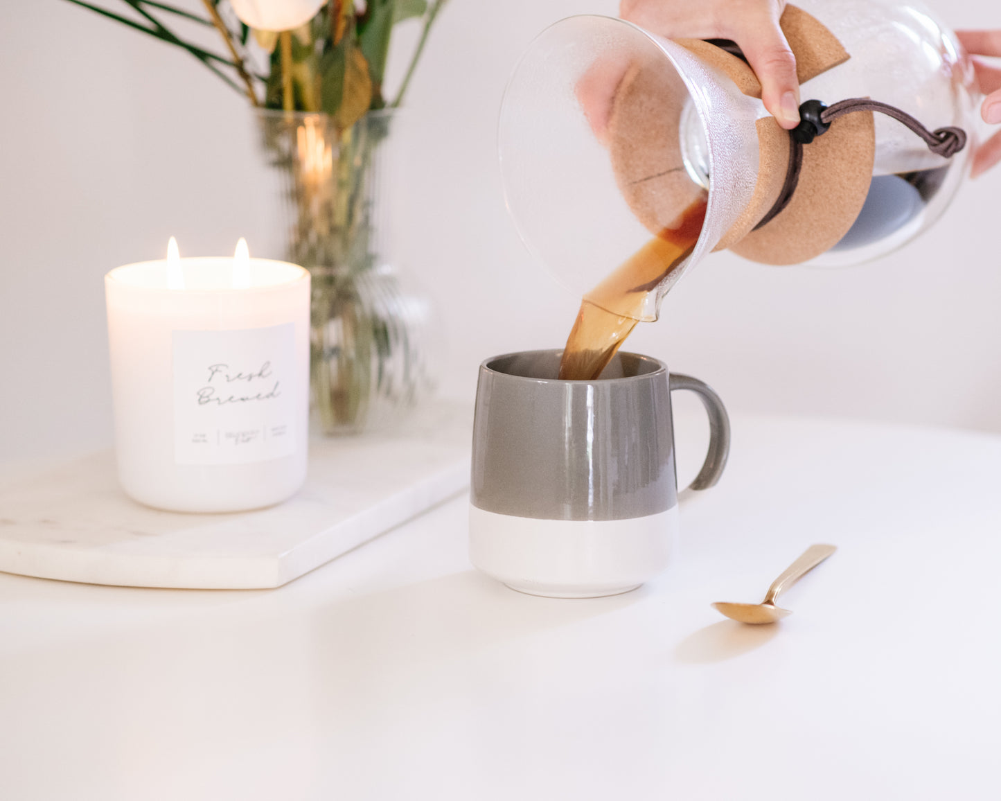 Deliciously Wickt glossy white 17 oz soy candle beside a coffee pot on a white table.