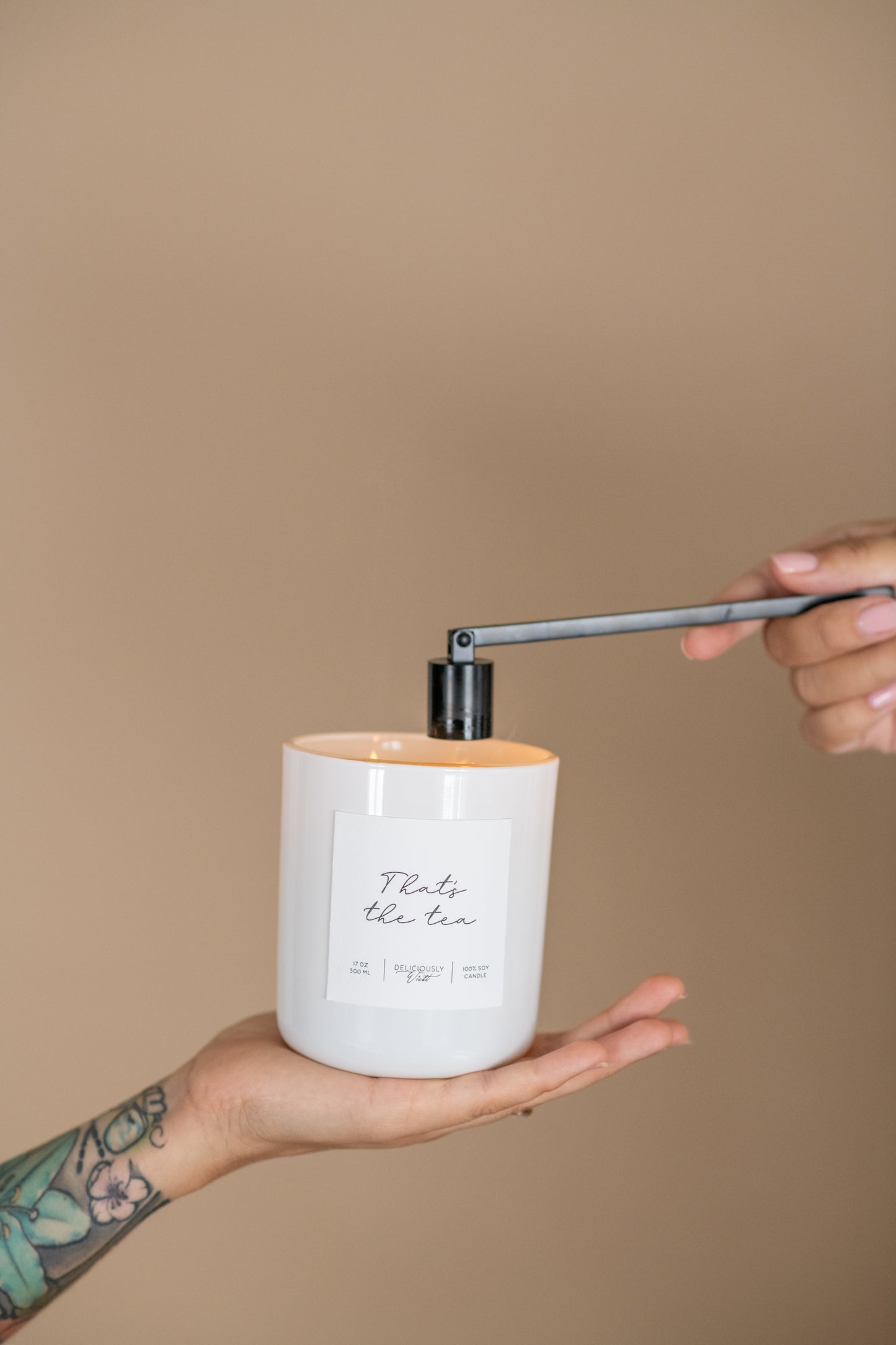 Deliciously Wickt glossy white 17 oz soy candle held in one hand while against a neutral background.