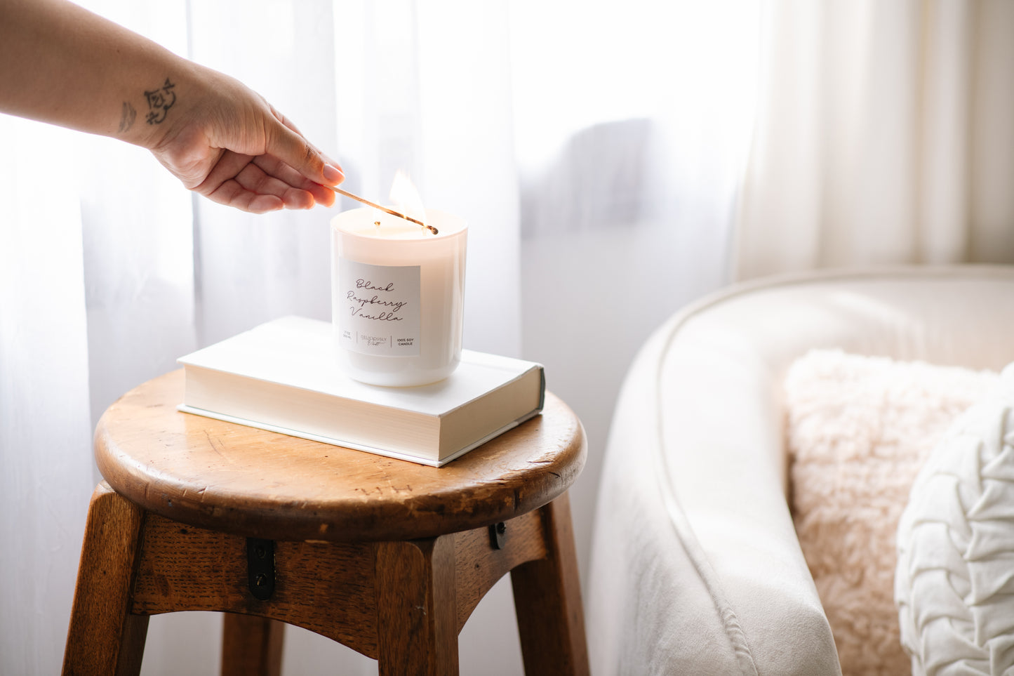 Deliciously Wickt glossy white 17 oz soy candle displayed on a wooden stool in a bright bedroom.