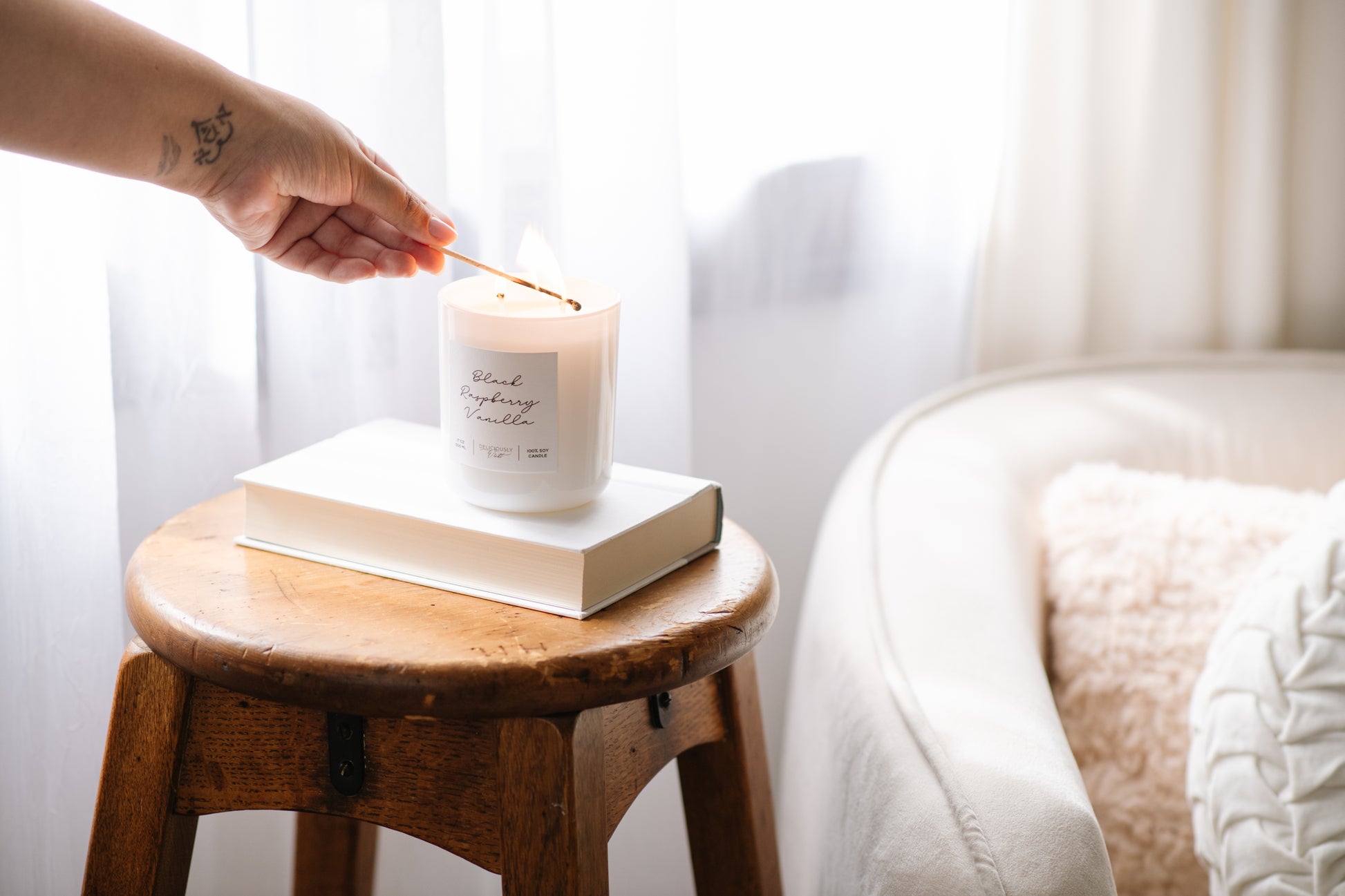 Deliciously Wickt glossy white 17 oz soy candle displayed on a wooden stool in a bright bedroom.