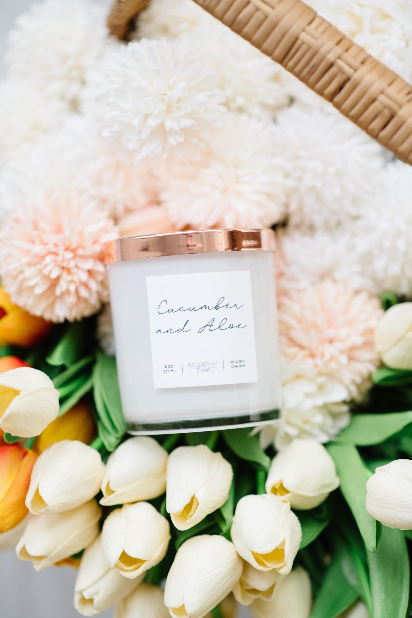 Deliciously Wickt glossy white 8 oz soy candle with rose gold lid surrounded by white and peach flowers.