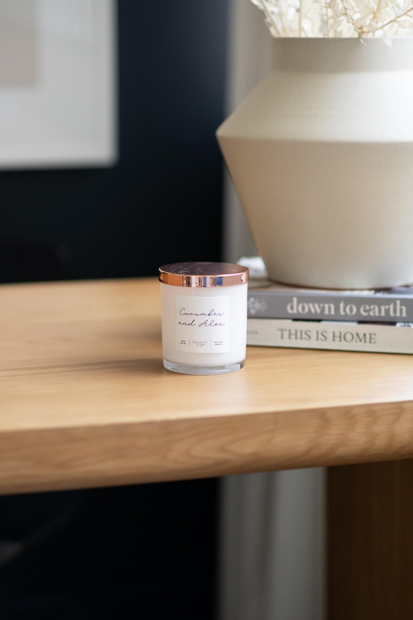 Deliciously Wickt glossy white 8 oz soy candle with rose gold lid displayed on a wooden table in a bright room.