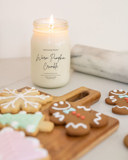 Deliciously Wickt Going, Going, Gone 16 oz mason jar soy candle lit beside iced cookies on a wooden board.