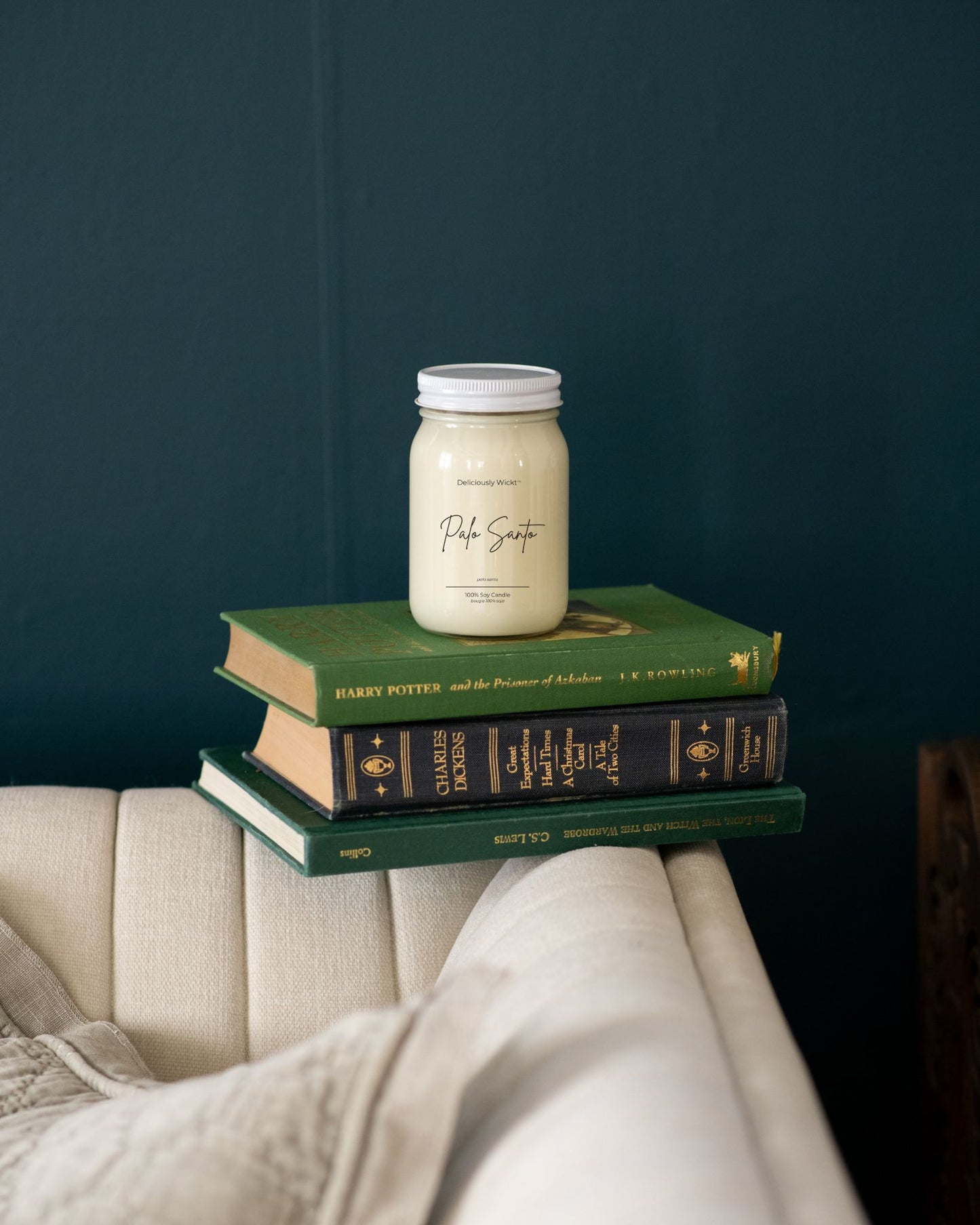 Deliciously Wickt Going, Going, Gone 16 oz mason jar soy candle displayed on stacked books against a dark wall.