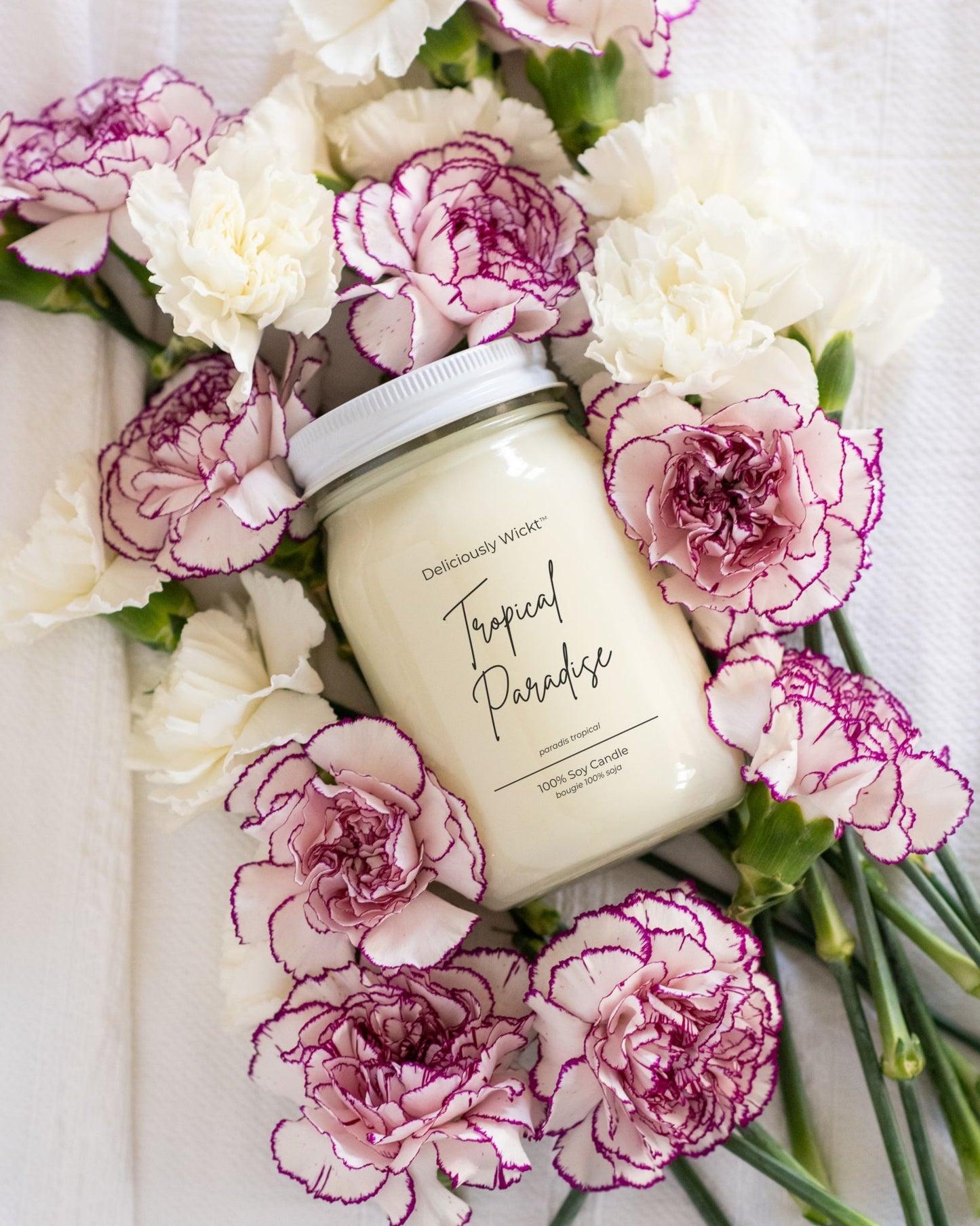 Deliciously Wickt Going, Going, Gone 16 oz mason jar soy candle surrounded by pink and white flowers.