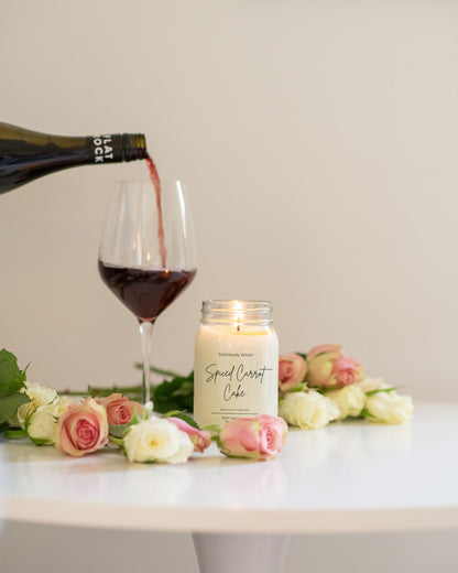 Deliciously Wickt Going, Going, Gone 16 oz mason jar soy candle styled beside flowers and a glass of wine.