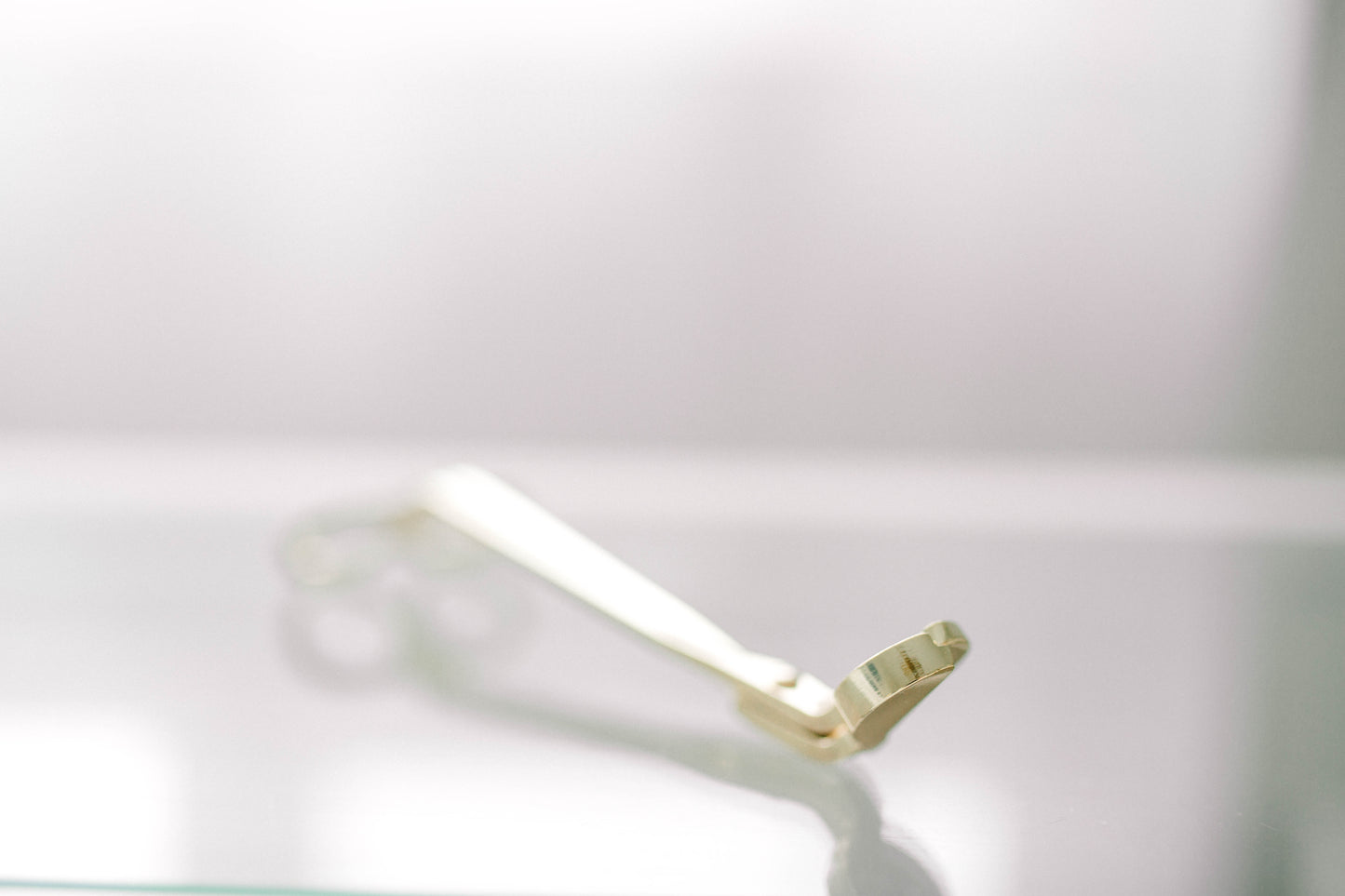 Deliciously Wickt gold metal candle wick trimmer displayed on a light background.