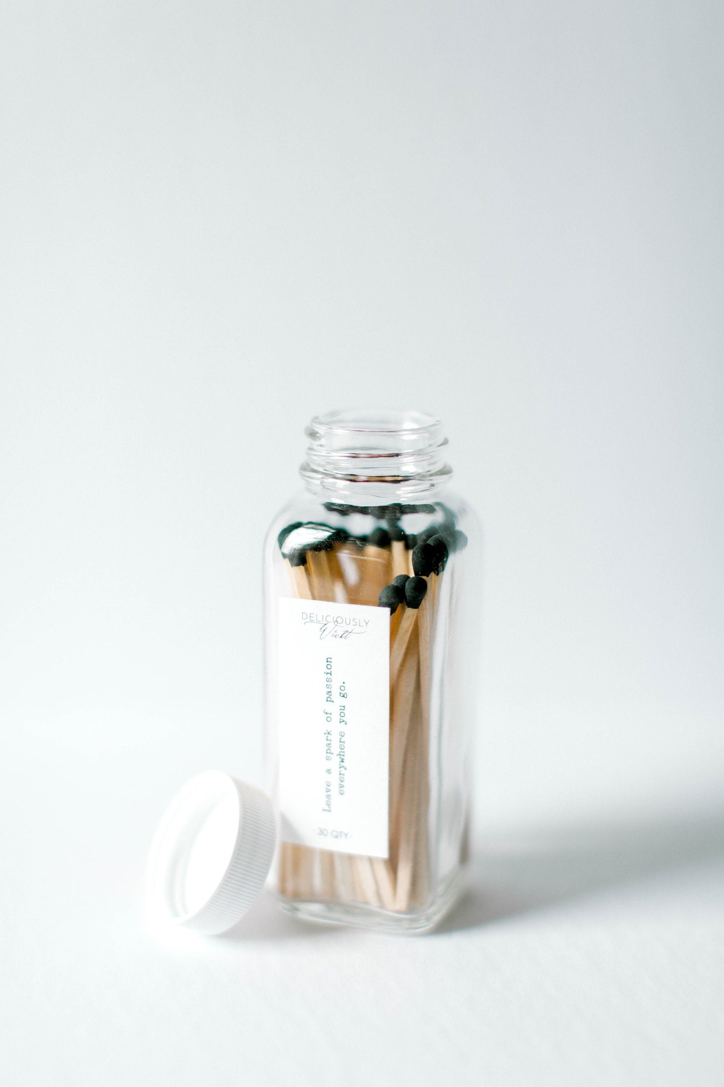 Deliciously Wickt green-tipped long stick safety matches standing in an open clear glass bottle with the lid beside it.