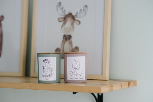 Deliciously Wickt Growth sage green and Be Still dusty rose 8 oz soy candles displayed together on a wooden nursery shelf beneath framed moose artwork.