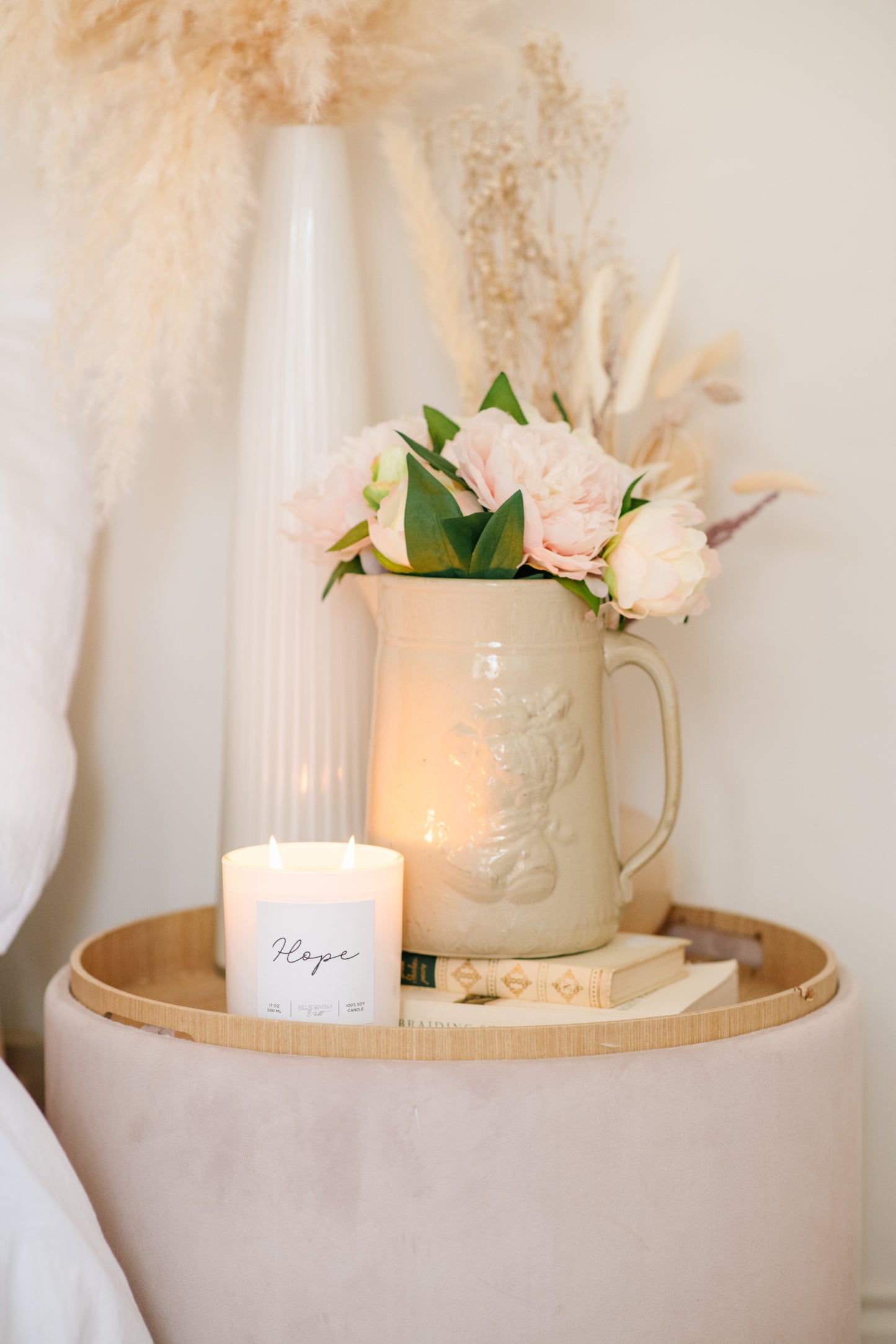Deliciously Wickt Hope/Love/Joy 17 oz soy candle displayed on a round table beside flowers.