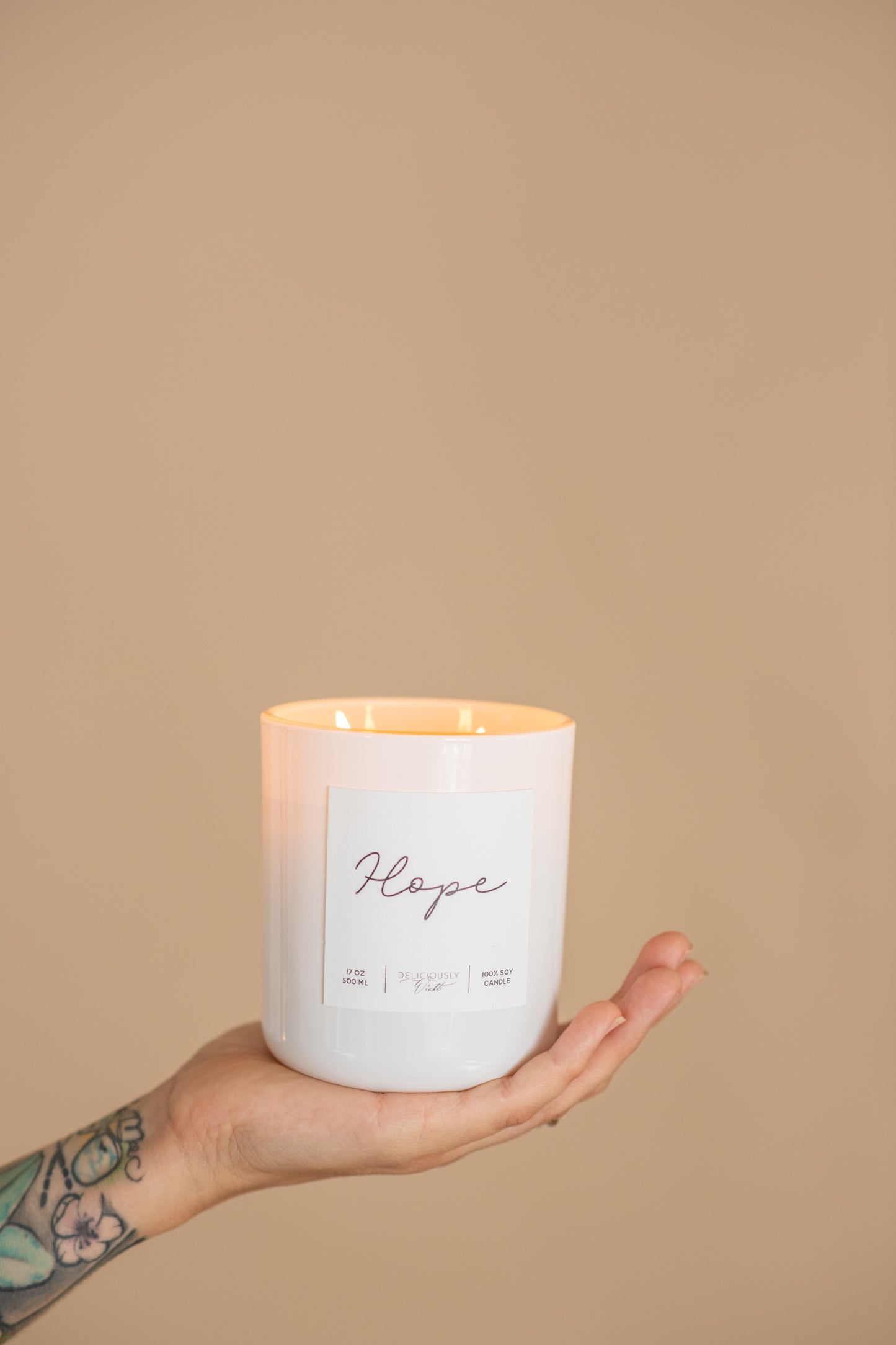 Deliciously Wickt Hope 17 oz soy candle held in one hand against a neutral background.