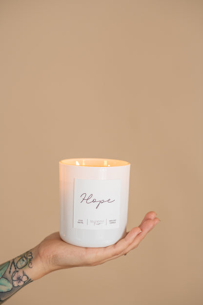 Deliciously Wickt Hope 17 oz soy candle held in one hand against a neutral background.