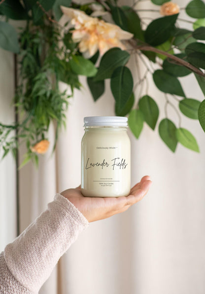 Deliciously Wickt Lavender Fields 16 oz mason jar soy candle held in one hand with green foliage in the background.