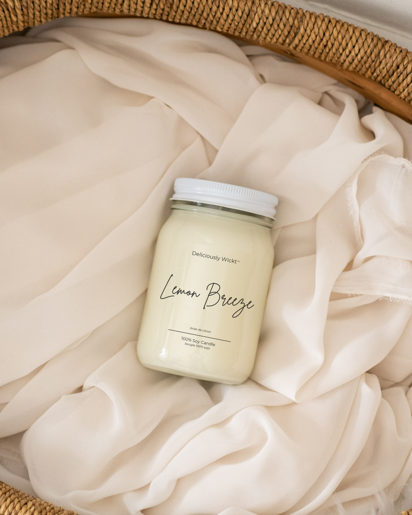 Deliciously Wickt Lemon Breeze 16 oz mason jar soy candle resting on soft cream fabric inside a woven basket.