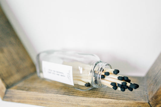 Deliciously Wickt long stick safety matches with black tips spilling from a clear glass match bottle on a wooden surface.