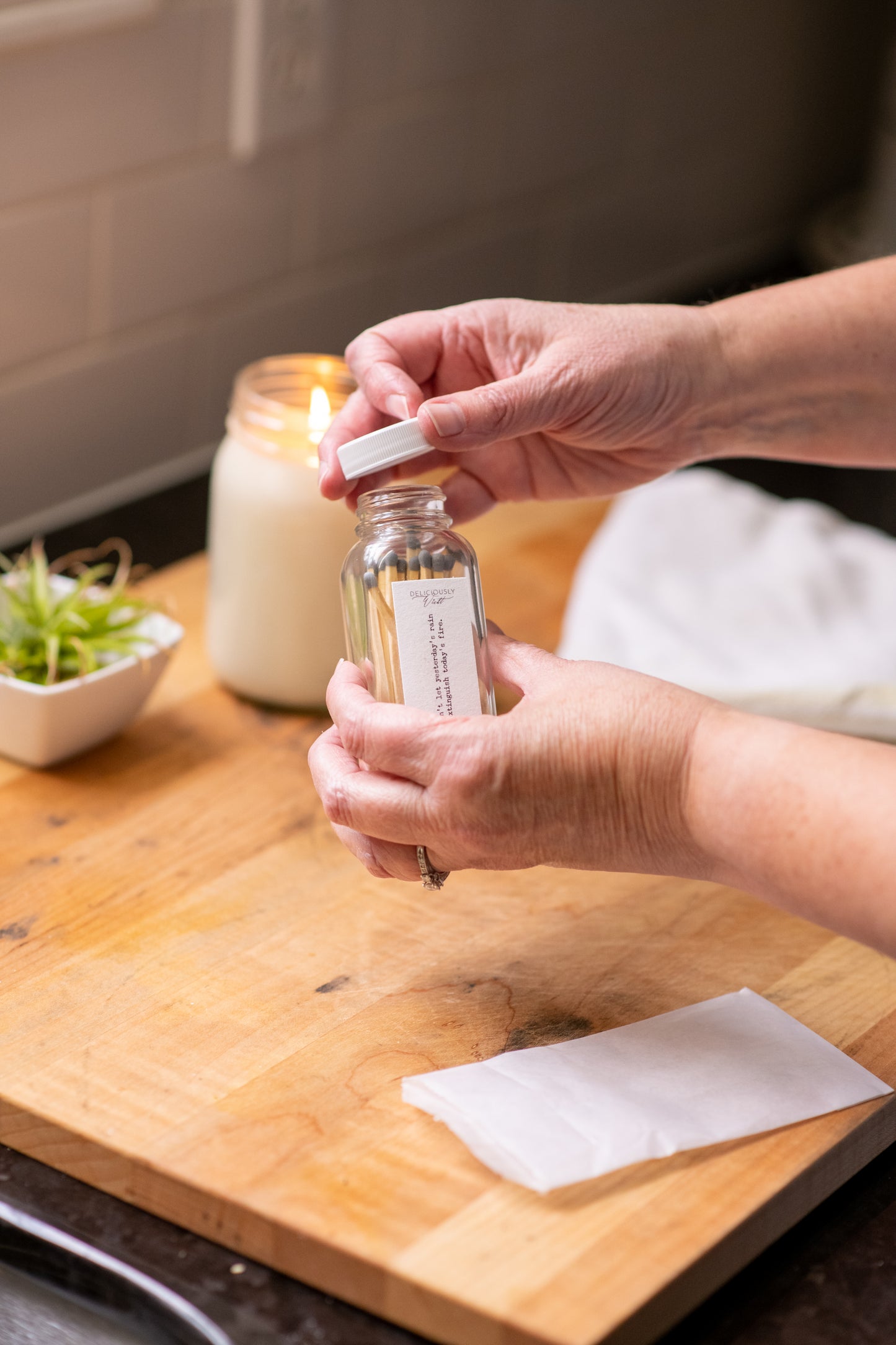 Deliciously Wickt long stick safety matches being removed from a clear glass match bottle beside a candle.