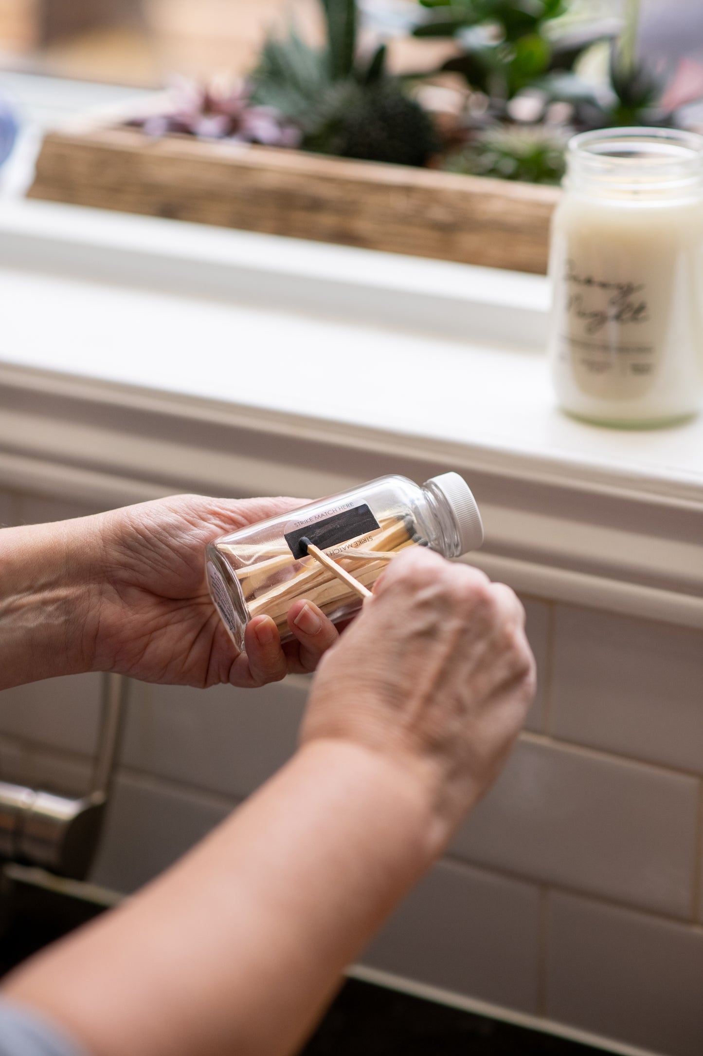 Deliciously Wickt long stick safety match being struck on the strike strip of a clear glass match bottle.