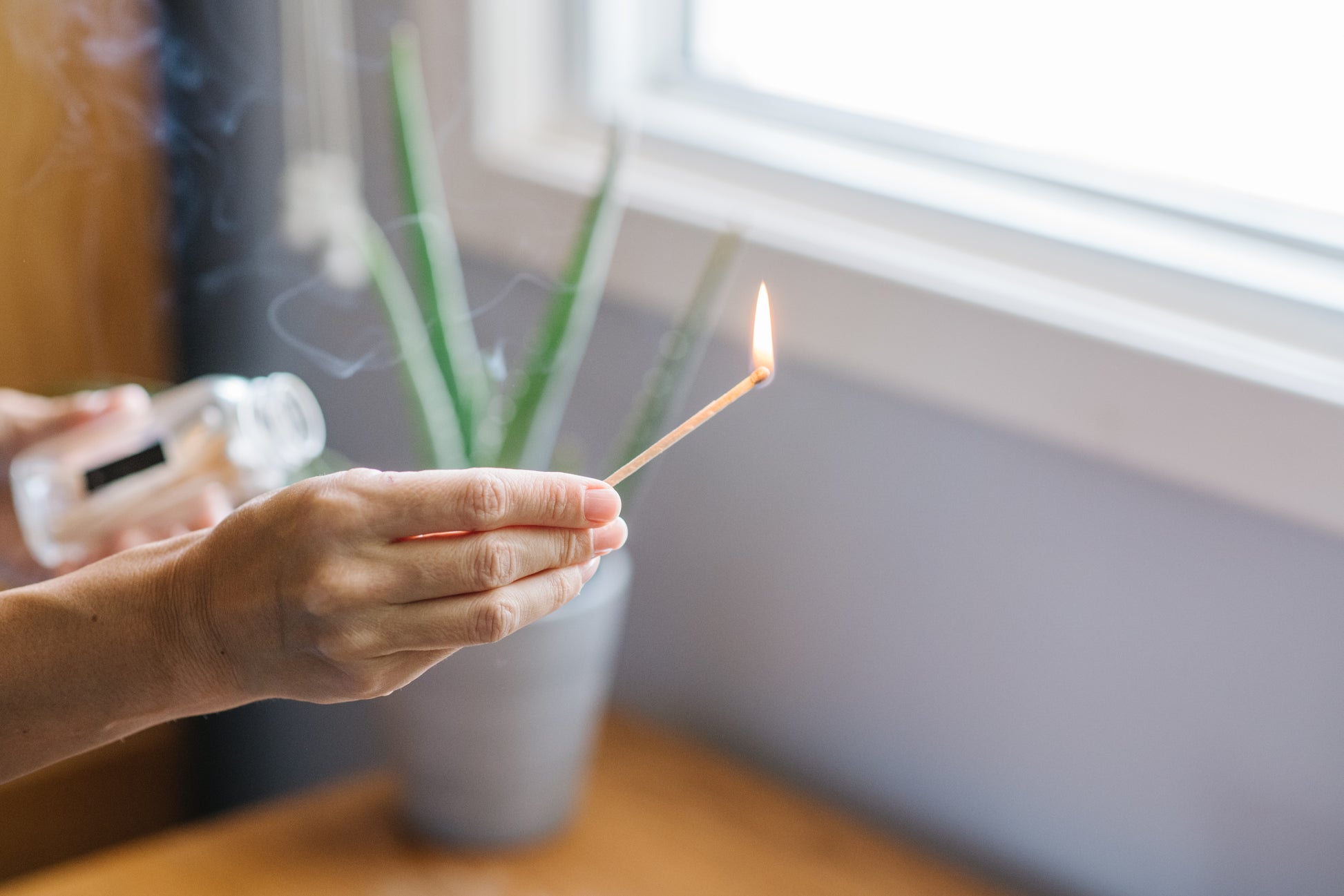 Deliciously Wickt long stick safety match burning beside a clear glass match bottle and houseplant.