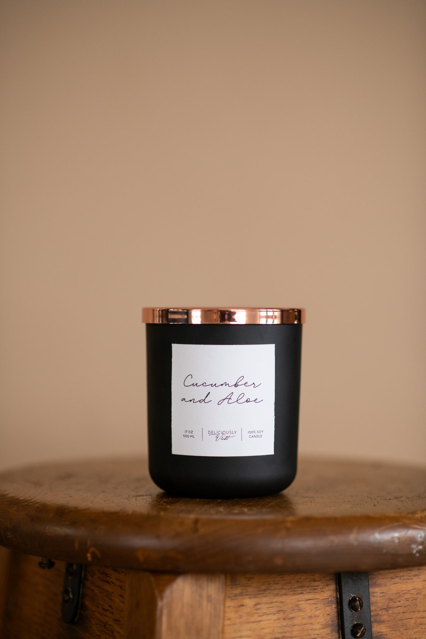 Deliciously Wickt matte black 17 oz soy candle displayed on a bathroom counter beside gold fixtures.