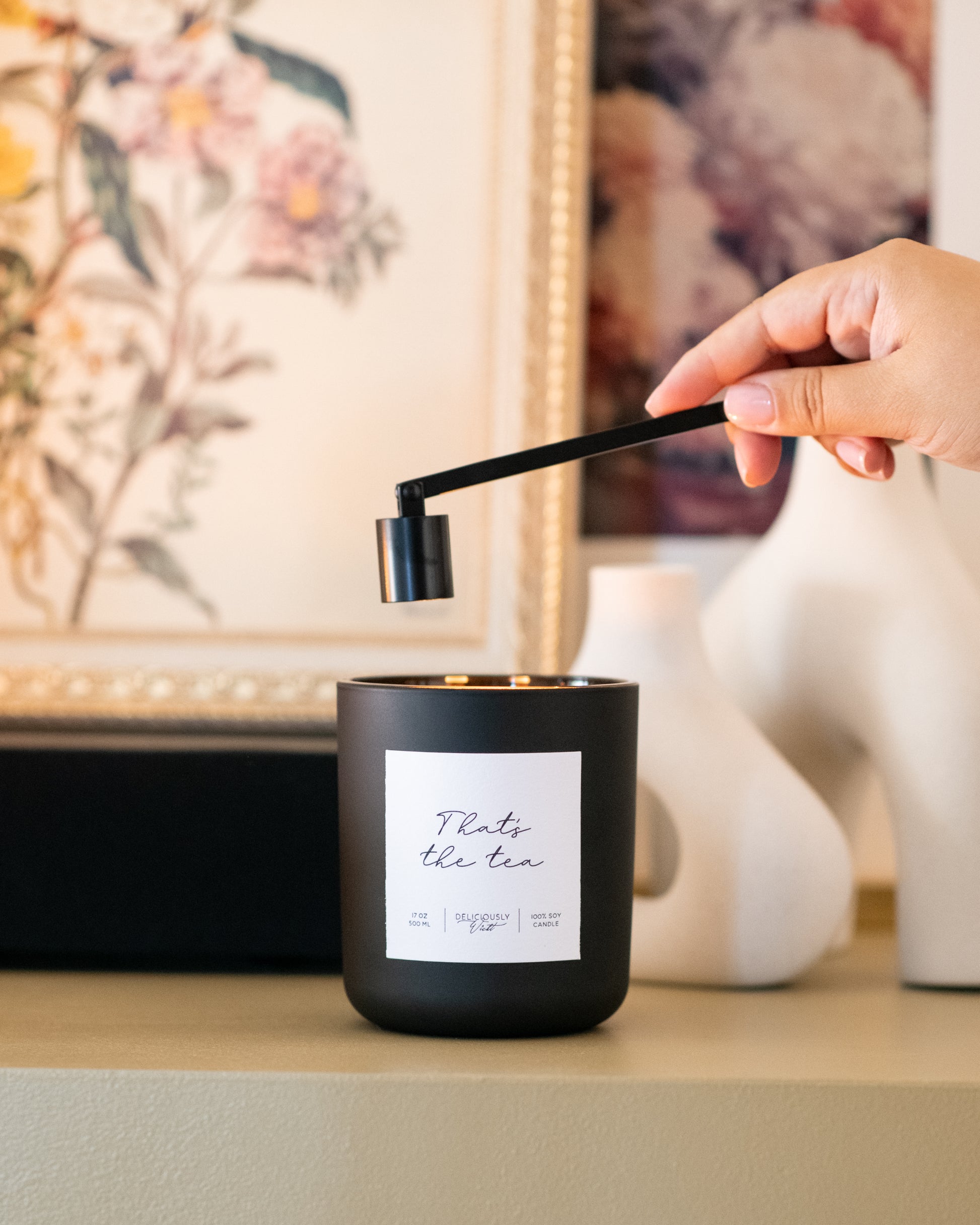 Deliciously Wickt matte black 17 oz soy candle being snuffed out on a table in a styled room.