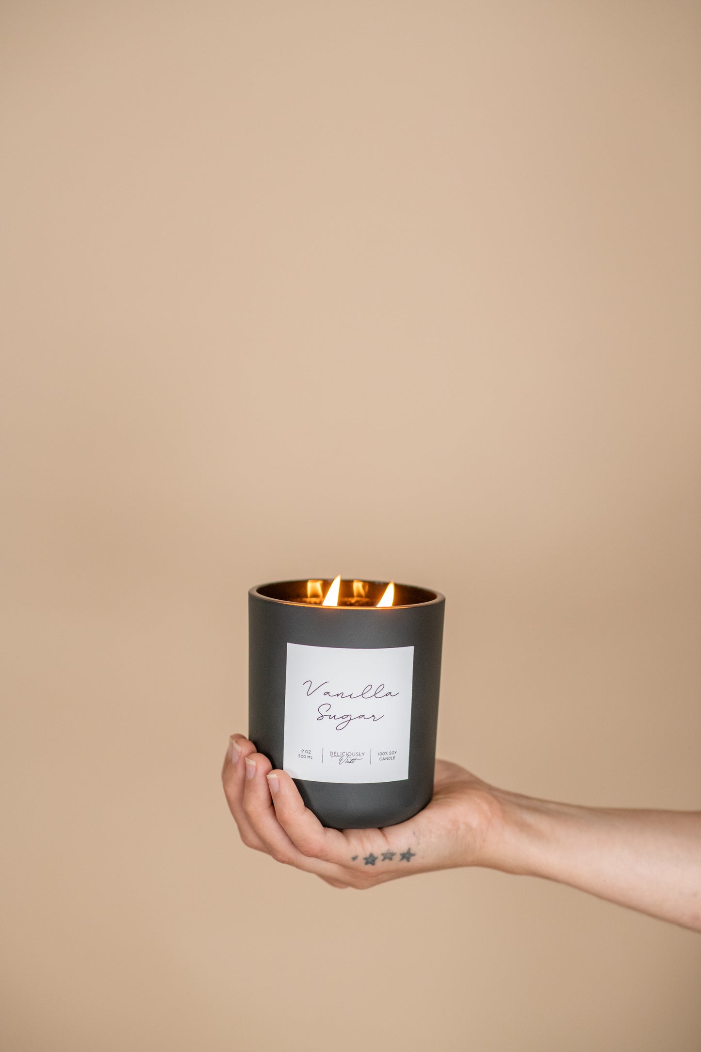 Deliciously Wickt matte black 17 oz soy candle held in one hand against a neutral background