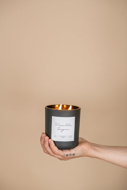 Deliciously Wickt matte black 17 oz soy candle held in one hand against a neutral background