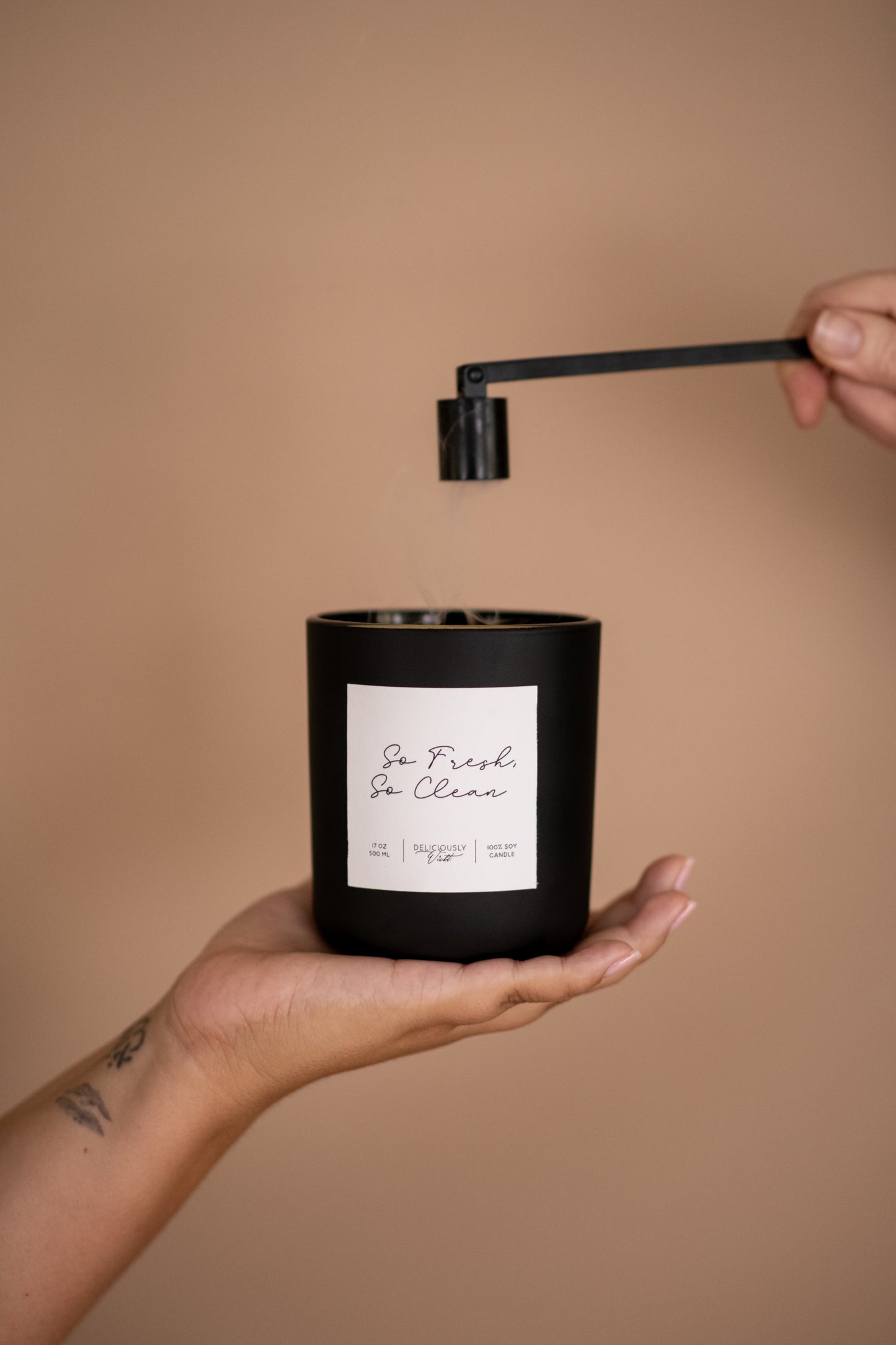 Deliciously Wickt matte black 17 oz soy candle held in one hand while being snuffed out.