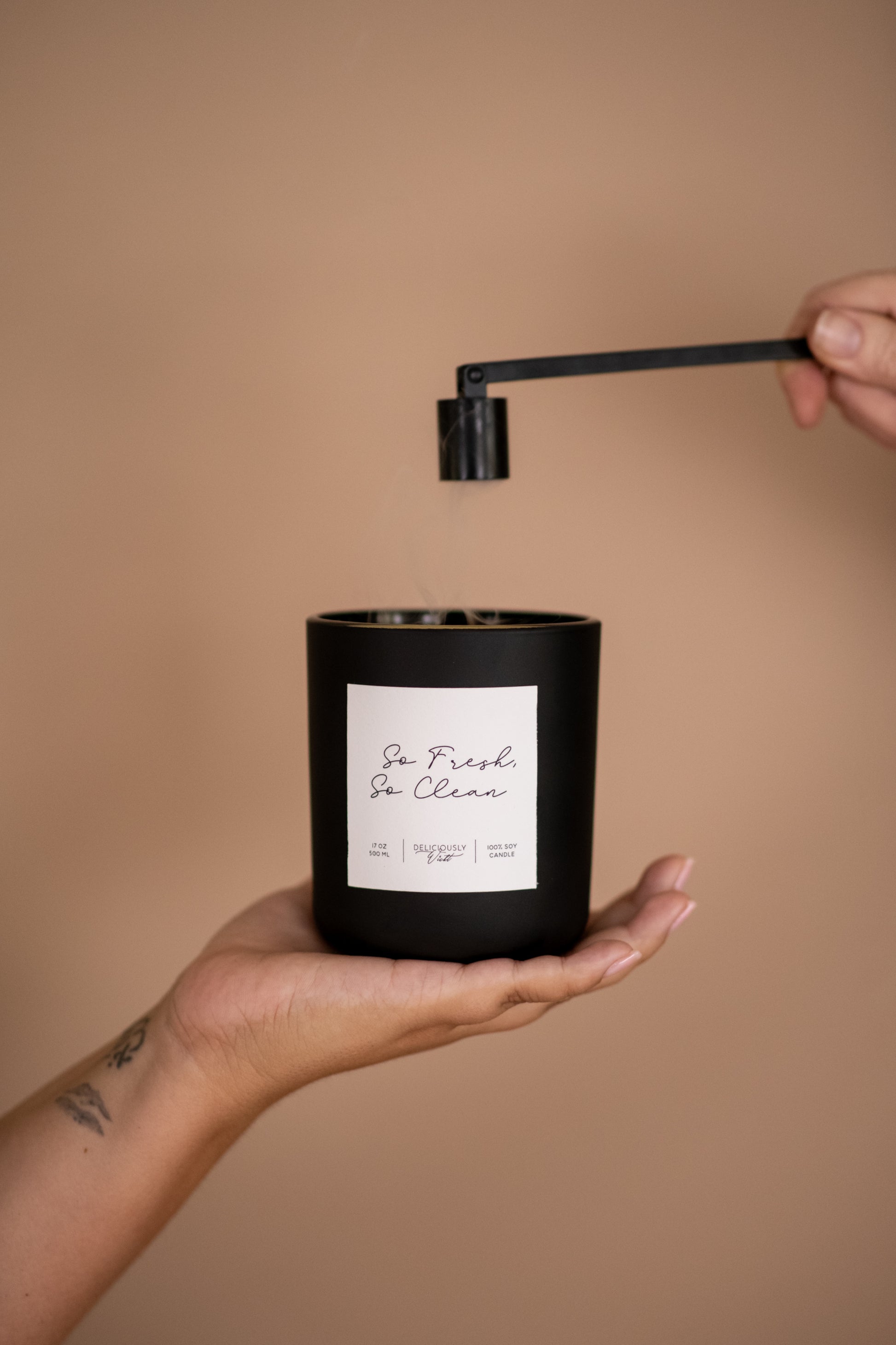 Deliciously Wickt matte black 17 oz soy candle held in one hand while being snuffed out.
