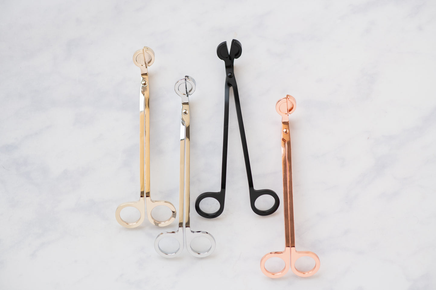 Deliciously Wickt metal candle wick trimmers in assorted finishes displayed on a light background.