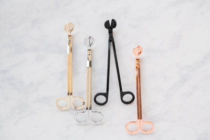 Deliciously Wickt metal candle wick trimmers in assorted finishes displayed on a light background.